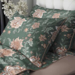 Green floral bedding set with large peach-and-cream flowers and leaves on pillowcases and sheets, a decorative bed setup.