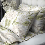 Decorative pillows and duvet cover with pale green and cream hydrangea floral pattern on white bedding.