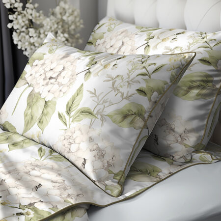 Decorative pillows and duvet cover with pale green and cream hydrangea floral pattern on white bedding.