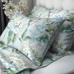 Decorative pillows with a blue-green floral botanical pattern on a light bedspread.